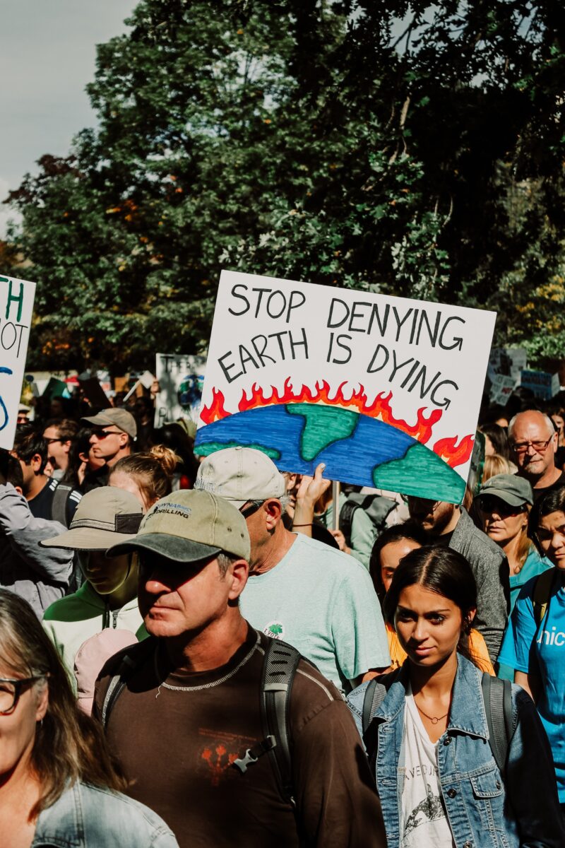 Climate change protesters holding a picket sign that reads: Stop Denying, Earth is Dying.